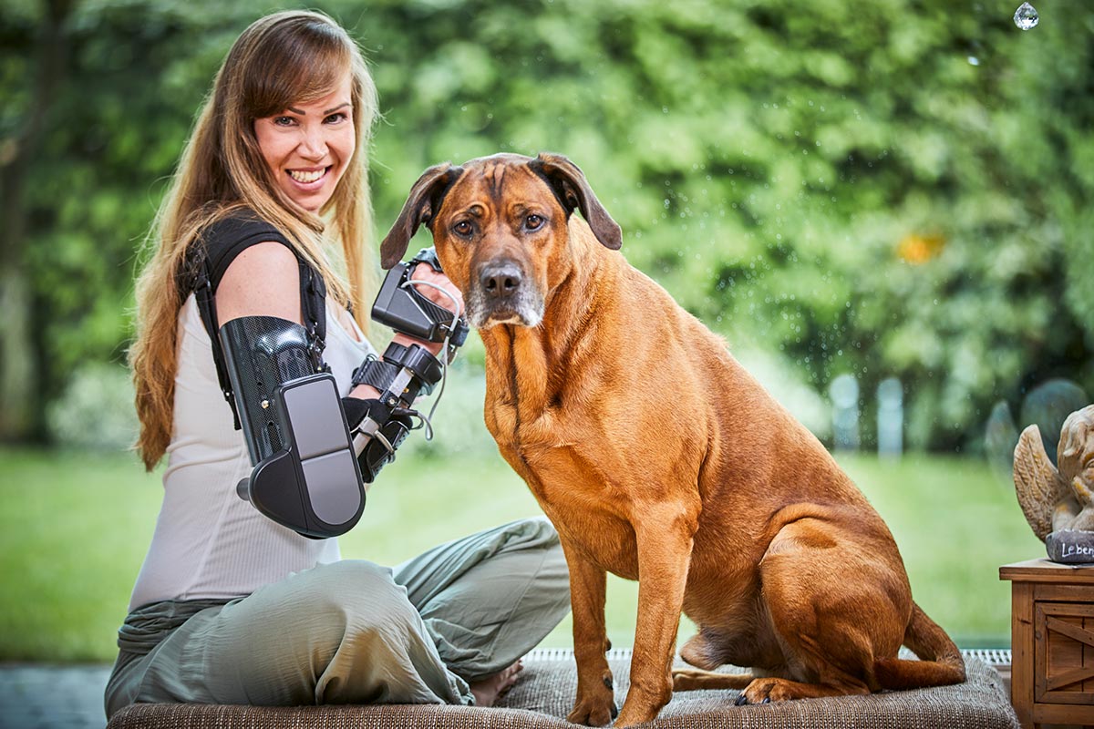 Trägerin mit Myopro Armorthese sitzt in Schneidersitz neben ihrem Hund.