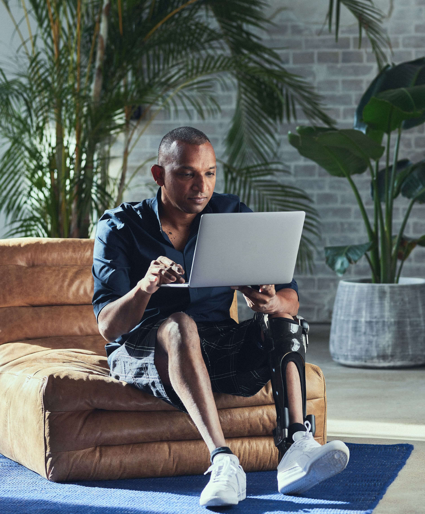 Träger einer Ottobock C-Brace Beinorthese sitzt entspannt auf einem Sessel und arbeitet am Laptop.