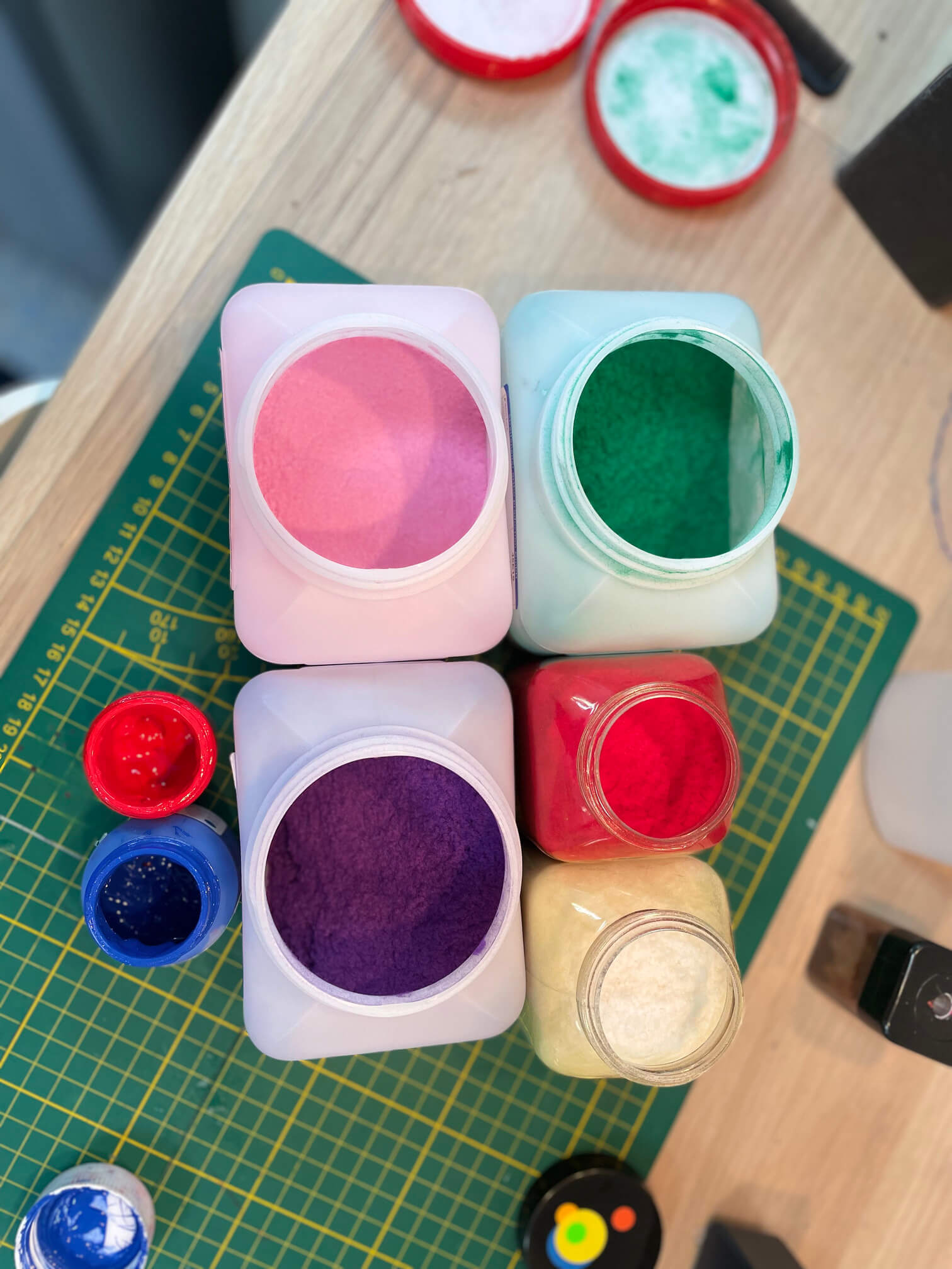 Pigmente Silikon Herstellungsprozess geöffnete Kunststoffbehälter mit farbigem Pulver in Pink, Grün, Lila, Rot und Weiß auf einem Arbeitstisch mit Schneidmatte – Pigmente oder Füllstoffe zur Herstellung von Silikonprothesen.