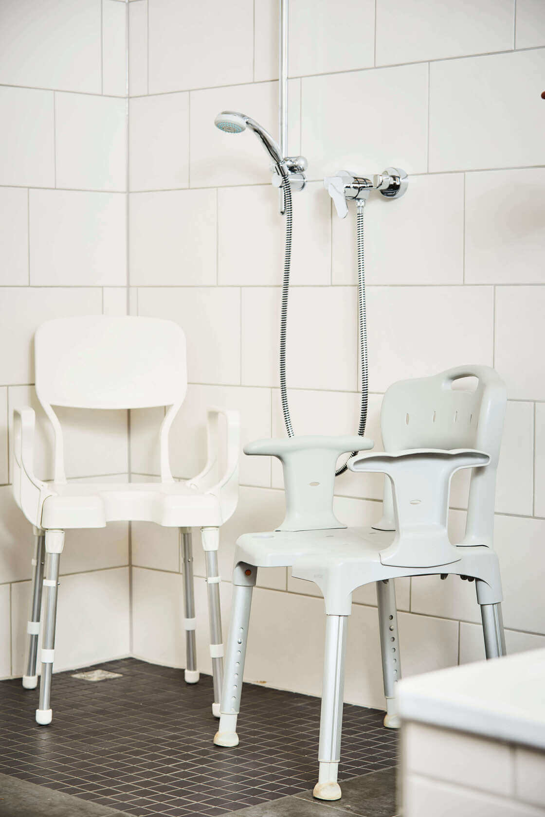 Zwei helle Duschstühle stehen beispielhaft in einer Dusche.