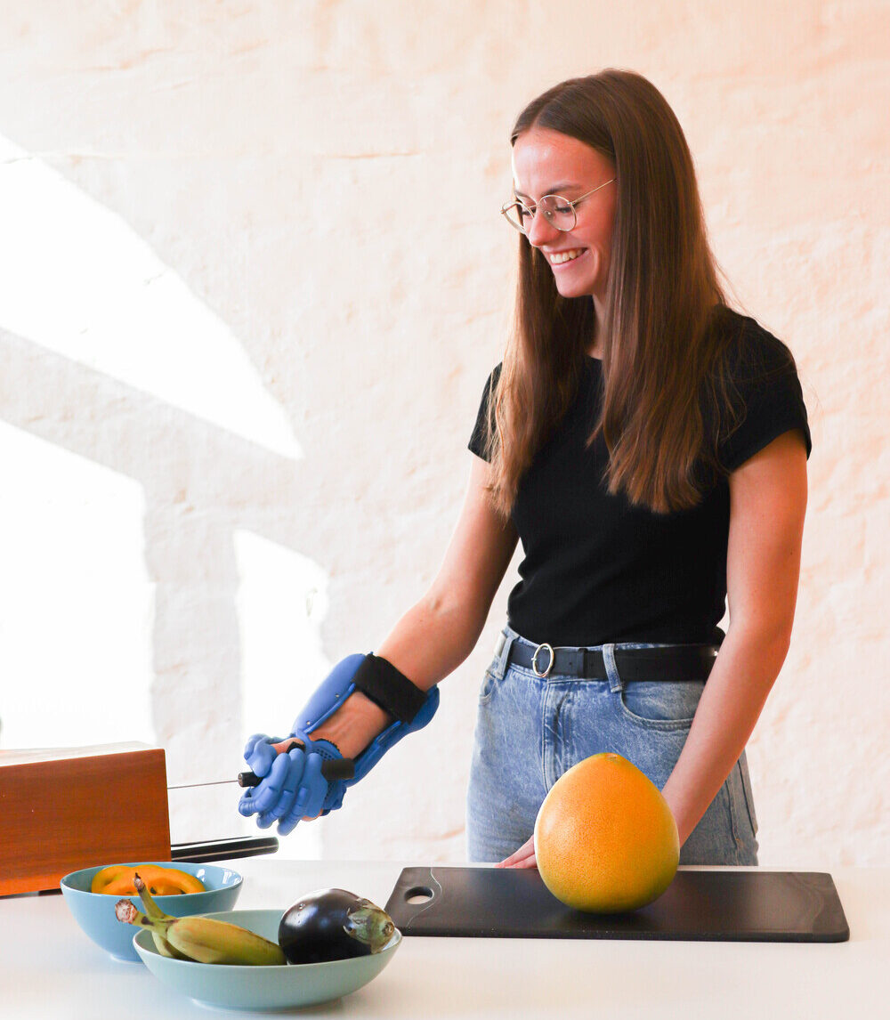 Trägerin der exomotion® hand one Orthese hält Messer um Obst zu schneiden.