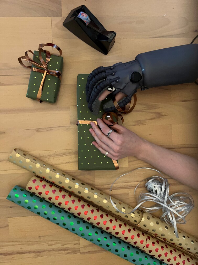 Vogelperspektive auf Hände, eine davon trägt Exomotion Hand One Orthese, die gerade Geschenke einpacken.