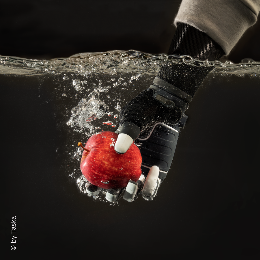 Taska Handprothese greift einen Apfel unter Wasser – illustriert die wasserdichte Funktionalität der Prothese bei alltäglichen Aufgaben.